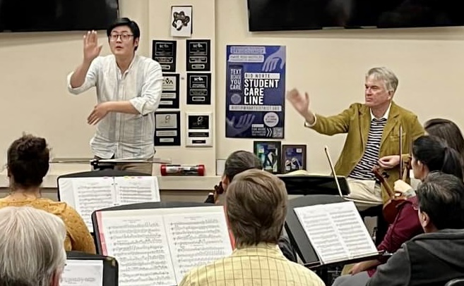 A young conductor and Brian Stone gesturing during an orchestra rehearsal